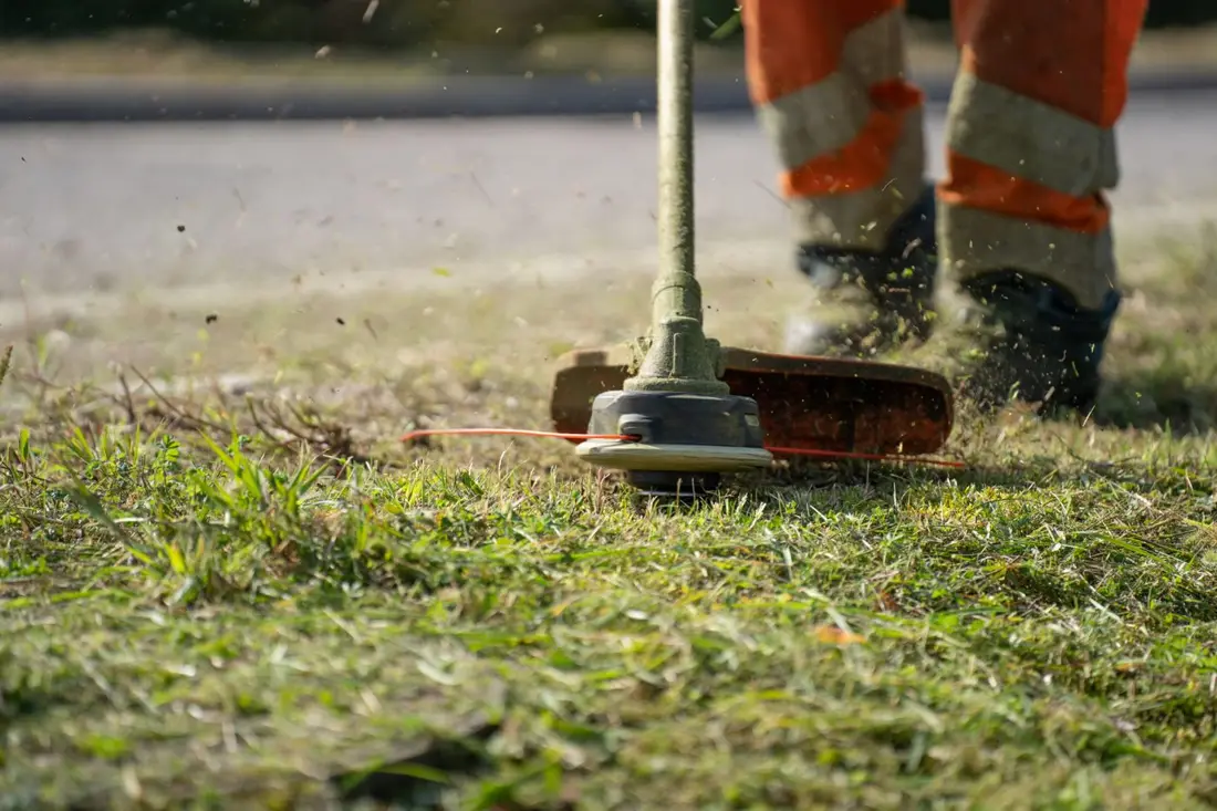 Lawn edging in Kelowna, powered trimmer cutting a clean grass edge along a sidewalk